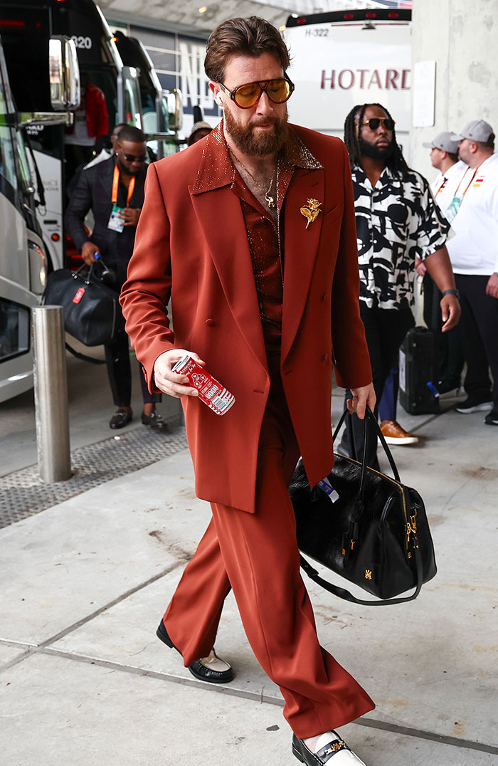 Man in a bold orange suit and sunglasses, holding a can and bag, showcasing a bizarre look at Super Bowl 2025.