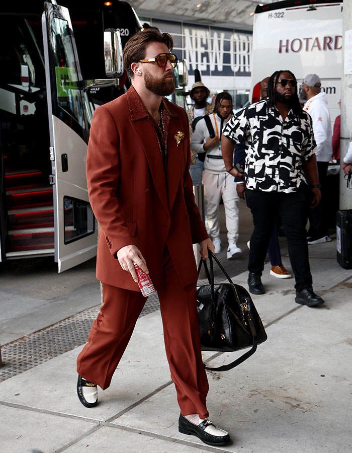 Man in stylish brown suit with sunglasses and a beard, stepping off a bus at Super Bowl 2025.