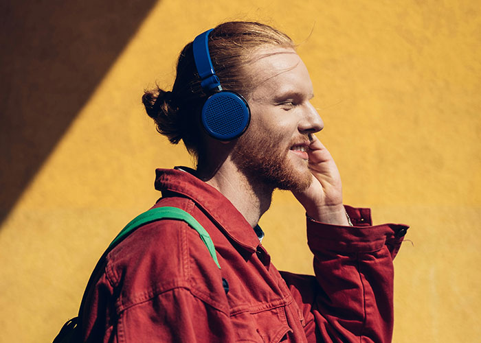 Person wearing headphones and a red jacket, walking outside in sunlight, embodying lifestyle tips for getting 10K steps daily.
