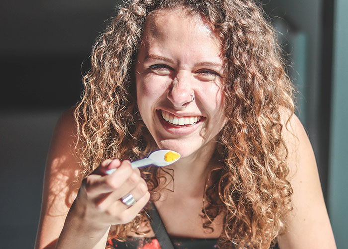 Smiling woman with curly hair holding a spoon, highlighting tips for getting 10K steps daily.