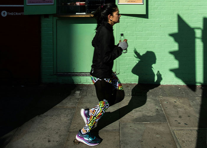 Person jogging outside a green building, holding a water bottle, focused on getting 10K steps daily.