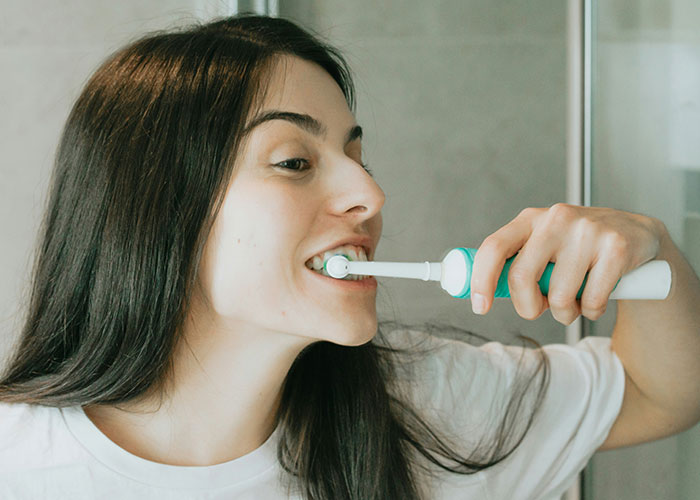Person brushing their teeth with an electric toothbrush, focusing on daily routine and healthy steps for well-being.