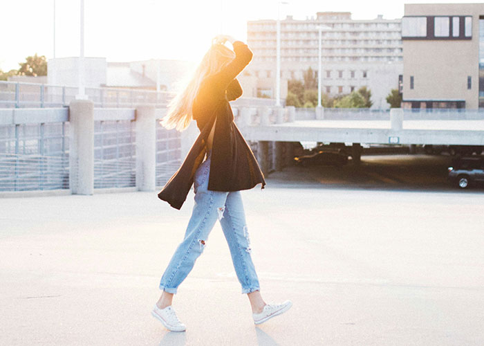 Woman walking briskly in casual attire on a sunny day, symbolizing tips for getting 10K steps daily.