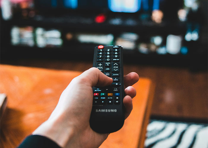 Hand holding a Samsung TV remote in a living room setting, likely after getting 10K steps in a day.