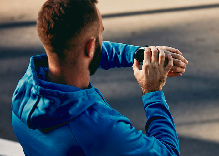 Man in a blue hoodie checking smartwatch, focusing on steps in a day.