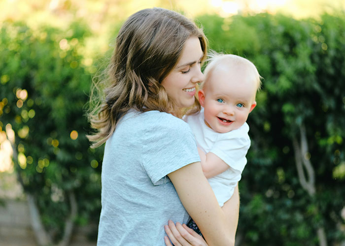 Woman holding a smiling baby outdoors, representing daily activity for getting 10K steps.