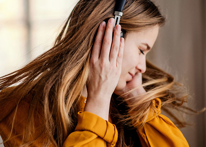 Woman enjoying music with headphones, smiling while moving, wearing a yellow top; a tip for getting 10K steps in a day.