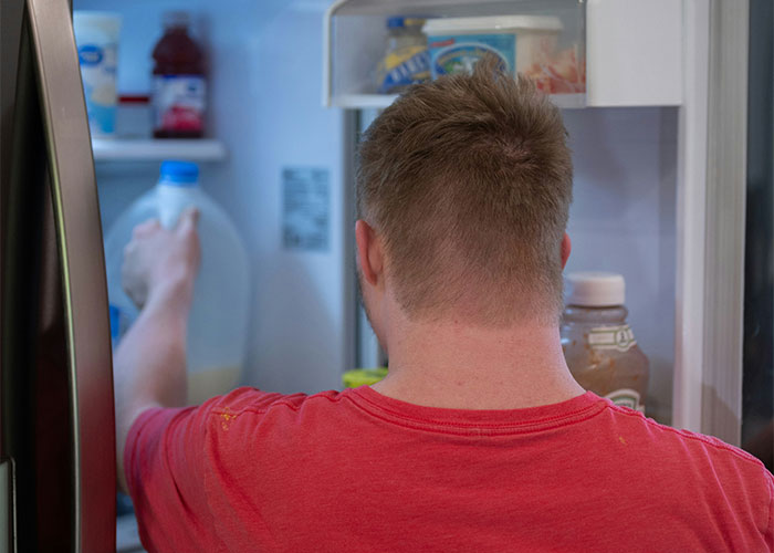 Man in a red shirt reaching into fridge, illustrating daily steps routine tips.