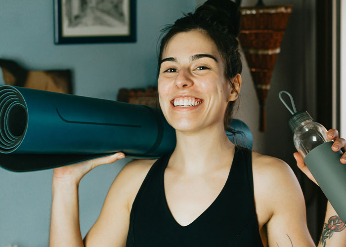 Smiling woman with yoga mat and water bottle, suggesting tips for getting 10K steps a day.