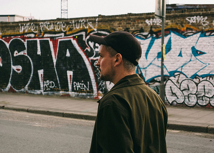 Man walking past graffiti-covered wall, wearing a cap and jacket, contributing to reaching 10K steps in a day.