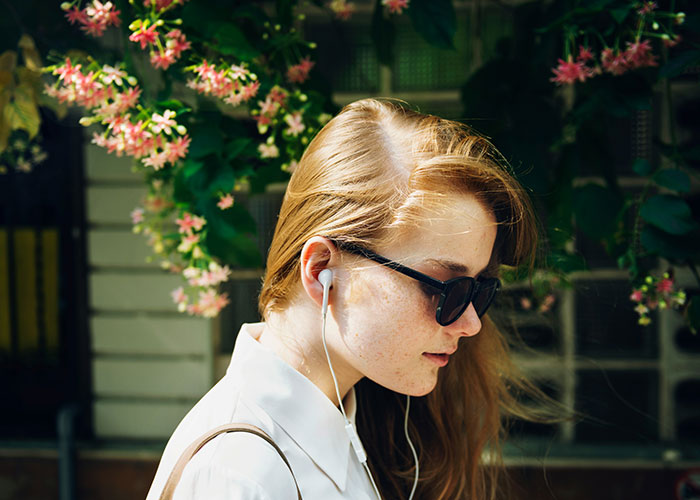 Person walks outdoors wearing earphones and sunglasses, seeking to reach 10K steps a day goal.