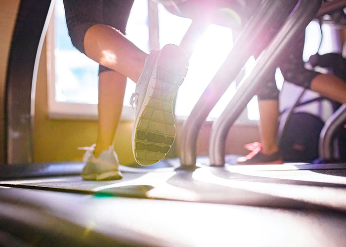 Feet in running shoes on a treadmill, sunlight streaming in, illustrating tips for getting 10K steps daily.
