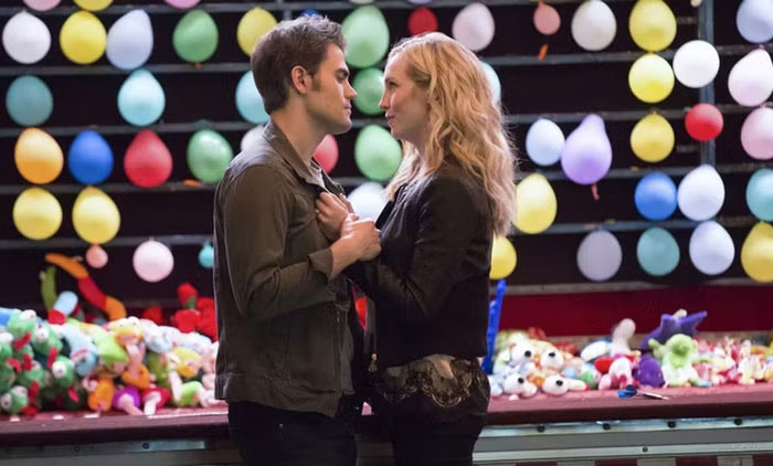 A TV couple holding hands at a carnival game, surrounded by balloons, lacking chemistry.