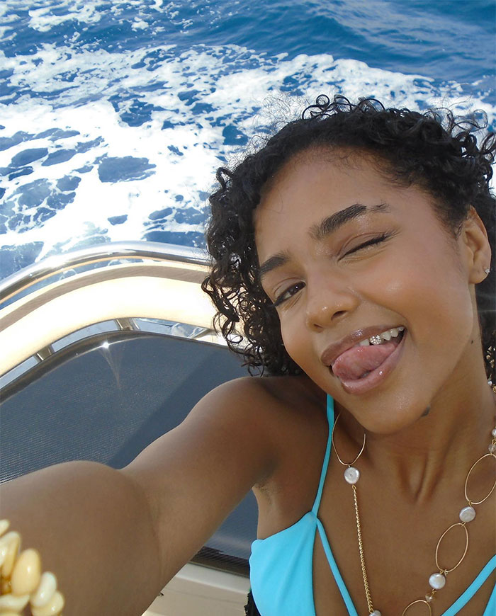 Tyla in a blue swimsuit on a boat, smiling and winking with the ocean in the background.