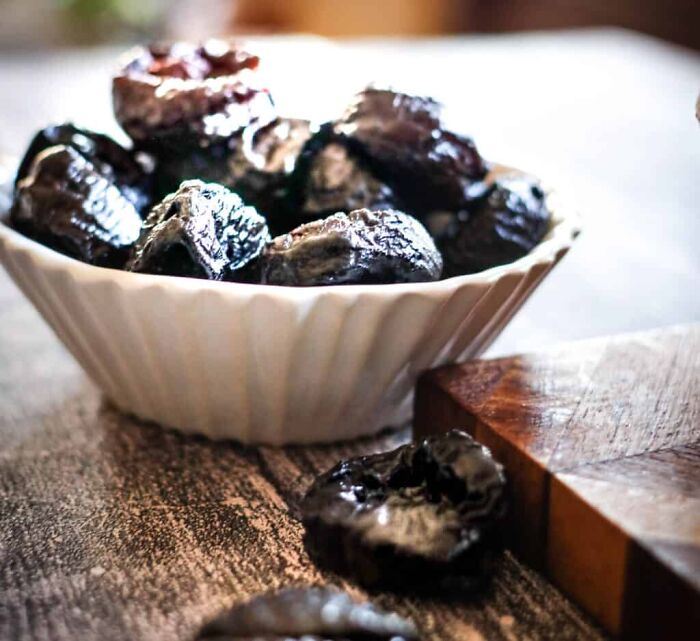 Bowl of prunes on a wooden surface, representing an unpopular opinion item in a rustic setting.