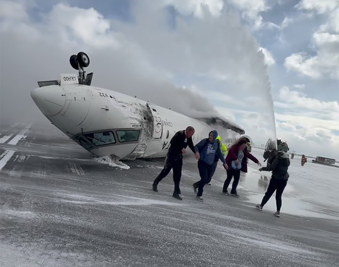 Passengers evacuate after an emergency landing with a plane overturned on the runway, smoke and rescue efforts visible.