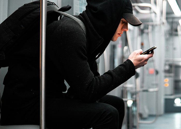 Person in a hoodie using a phone on public transport, emphasizing phone number privacy.