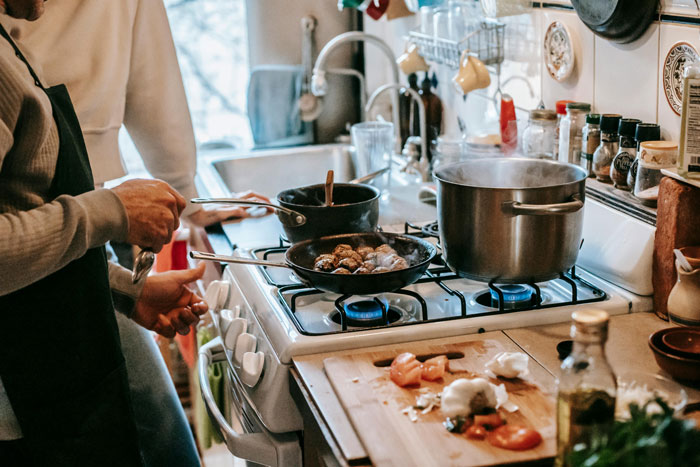 Two women cooking on a stove, with pots and ingredients, preparing a meal during a vacation.