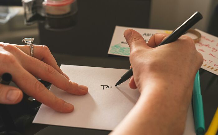 Writing a Valentine's card for kids, with a hand holding a black pen and addressing an envelope.