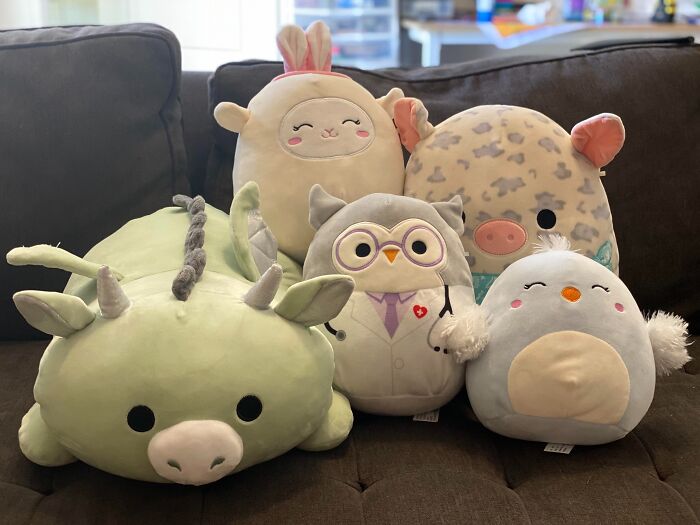 Plush toys for kids on Valentine's Day, featuring a unicorn, owl, and more, arranged on a brown couch.