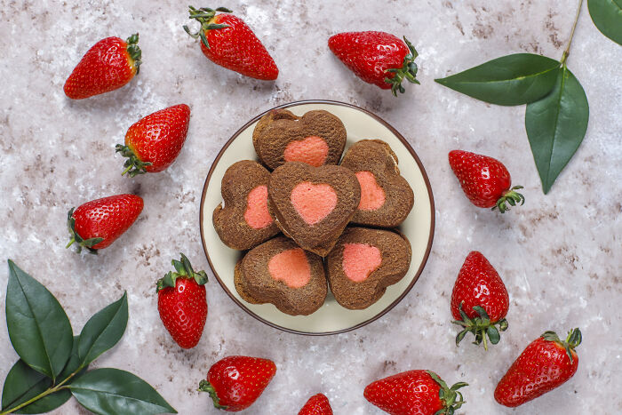 Heart-shaped cookies and strawberries arranged on a plate, perfect for kids on Valentine's Day.