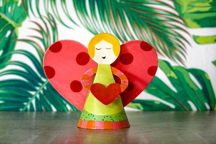 Colorful angel figurine with heart, perfect for Valentine's Day gifts for kids, in front of a tropical leaf background.