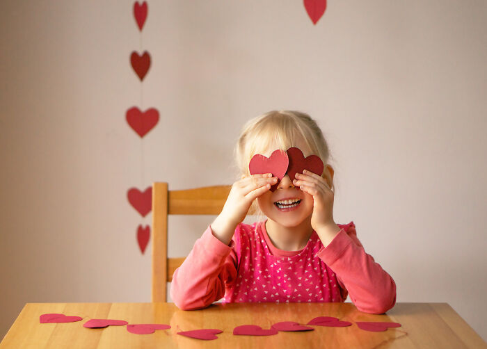 Child enjoying Valentine's Day with heart decorations, smiling at a table.