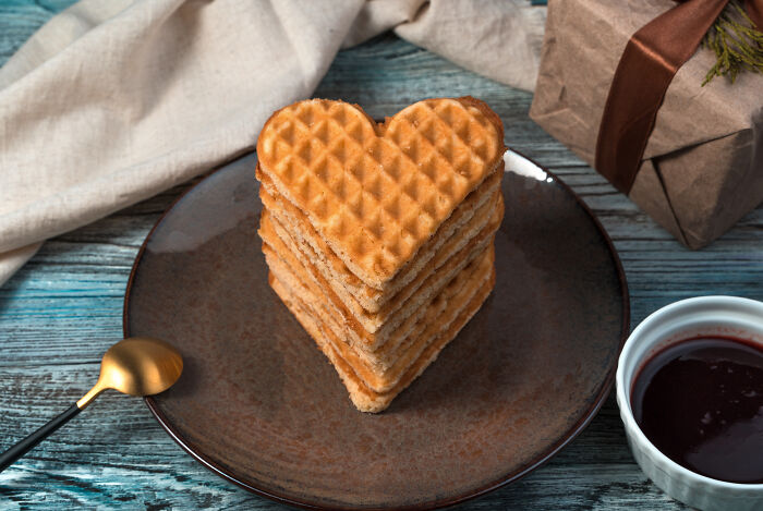 Heart-shaped waffles on a plate, perfect Valentine's gift for kids, with a gift box and a cup of chocolate sauce nearby.