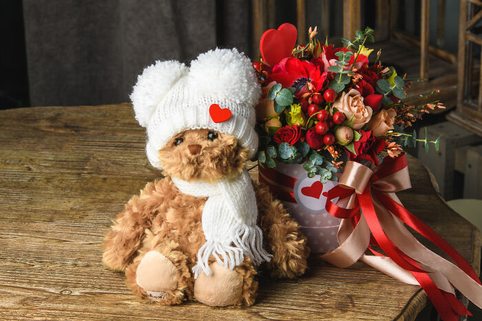 Teddy bear in a knitted hat next to a Valentine's floral arrangement, perfect gift idea for kids.