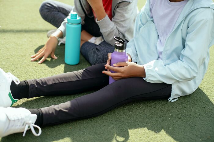 Kids sitting on grass, holding colorful water bottles, suitable for Valentine's gifts for children.