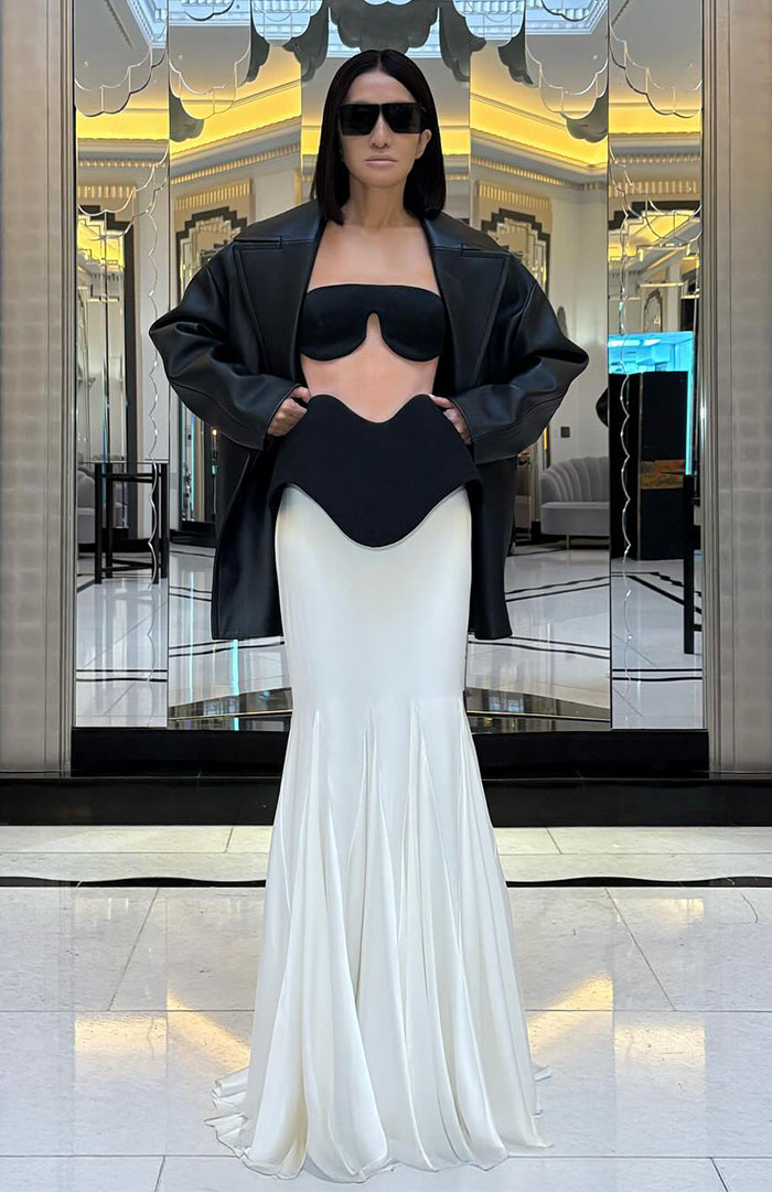 Person wearing Vera Wang's upside-down bra design with white skirt, black jacket, and sunglasses in an elegant setting. Person wearing Vera Wang's upside-down bra design with white skirt, black jacket, and sunglasses in an elegant setting.