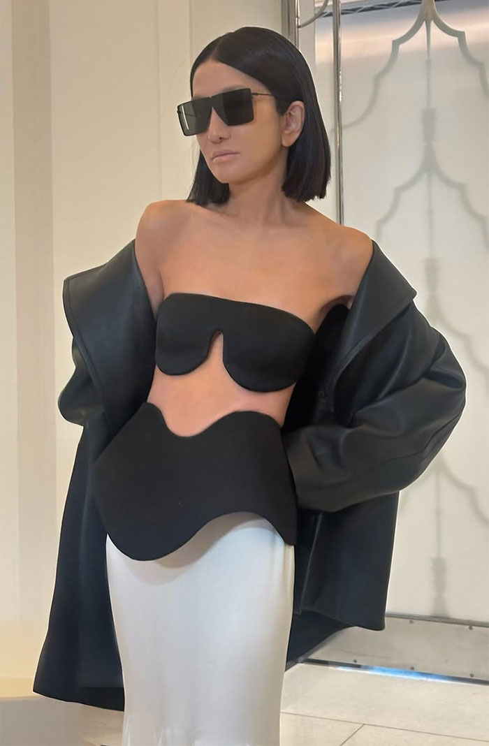 Person in sunglasses wearing Vera Wang's unique "upside-down bra" outfit with a black jacket indoors. Person in sunglasses wearing Vera Wang's unique "upside-down bra" outfit with a black jacket indoors.