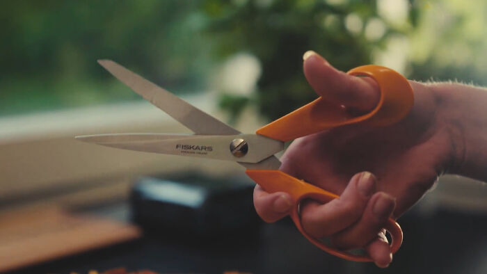 A hand holding durable orange-handled scissors, beautifully designed for longevity.