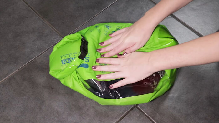 Hands closing a green travel compression bag on a tiled floor, showcasing an essential for easier and more peaceful travel.