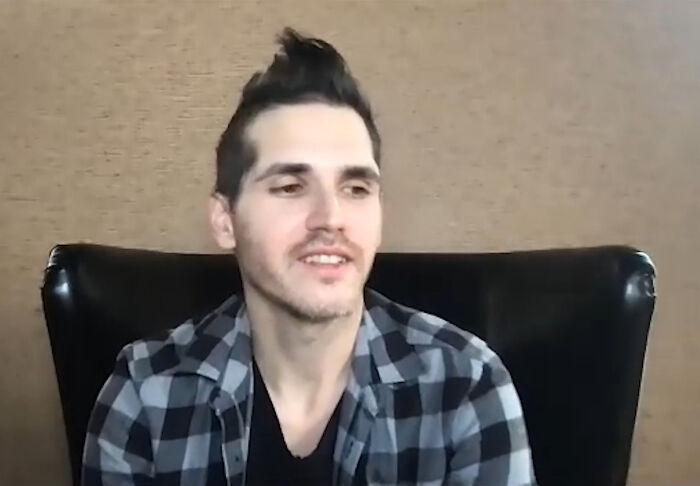 Young man in a checkered shirt, sitting on a black chair, talking about pop culture moments.