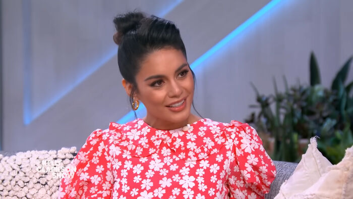 A person in a floral dress discussing pop culture moments on a talk show set.