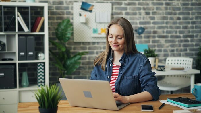 Woman with a prominent nose in a casual outfit working on a laptop in a cozy home office setting.
