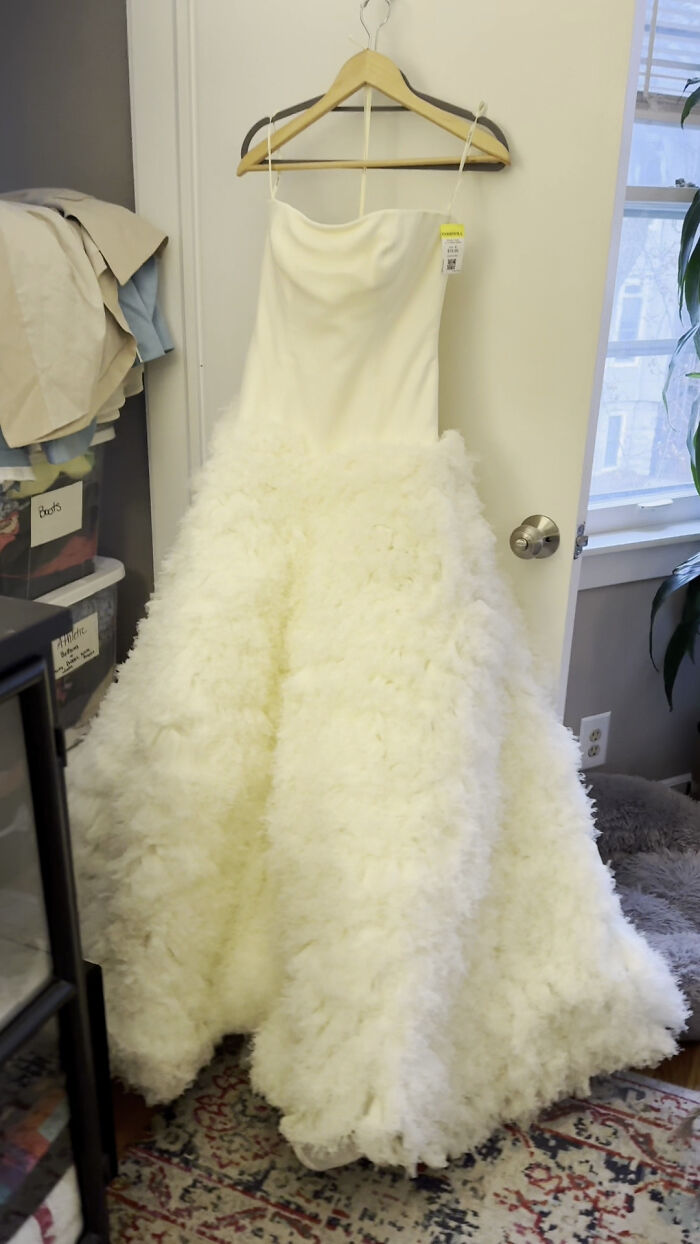 White wedding dress found at thrift store, hanging on a wooden hanger in a room.