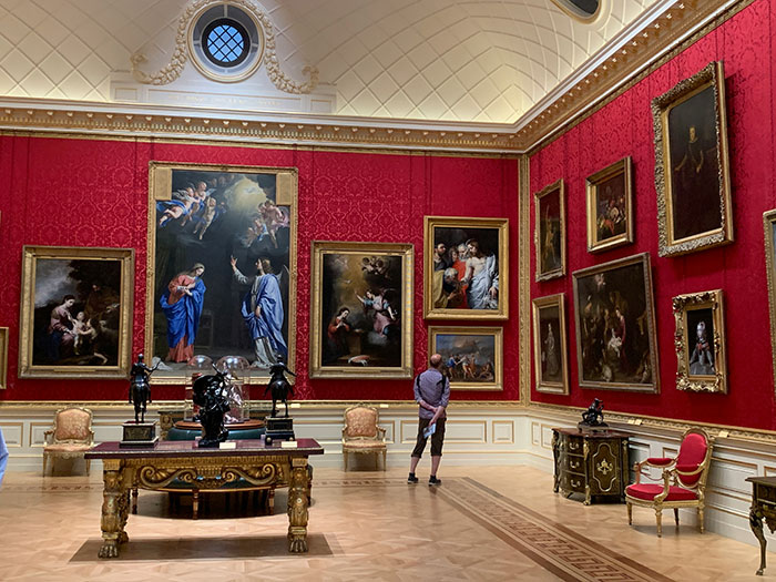 Luxurious art gallery room with red walls, featuring large classic paintings and ornate furniture, showcasing the super rich lifestyle.