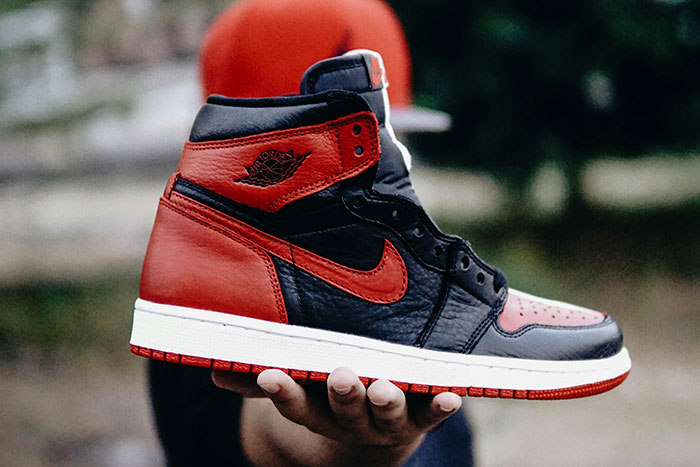 Luxury sneaker in red and black, hand-held in an outdoor setting, emphasizing things the rich can buy.