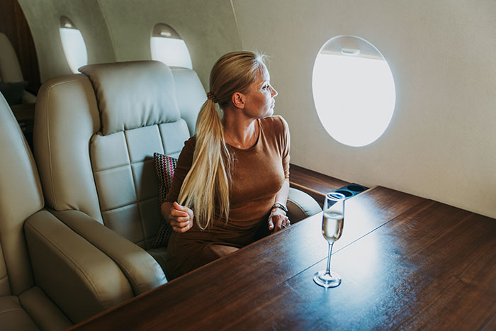 A woman enjoying a luxurious private jet, gazing out the window with a glass of champagne, showcasing things money can buy.
