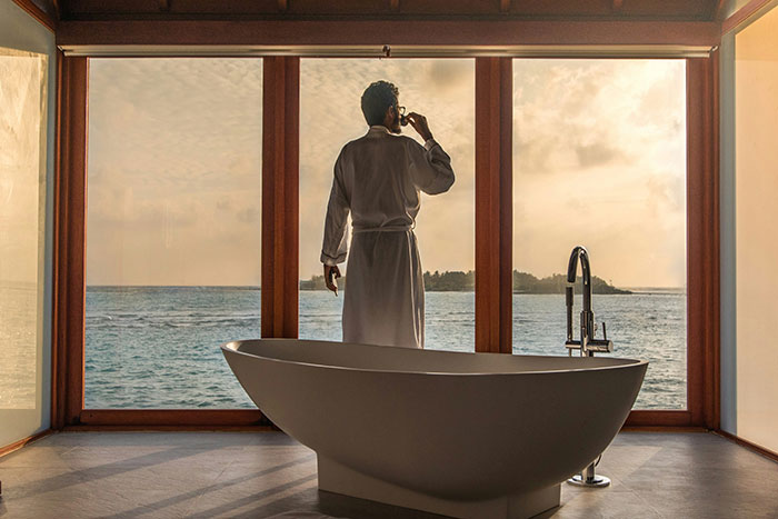 Person in luxury bathroom with ocean view, sipping drink, highlighting super rich lifestyle.