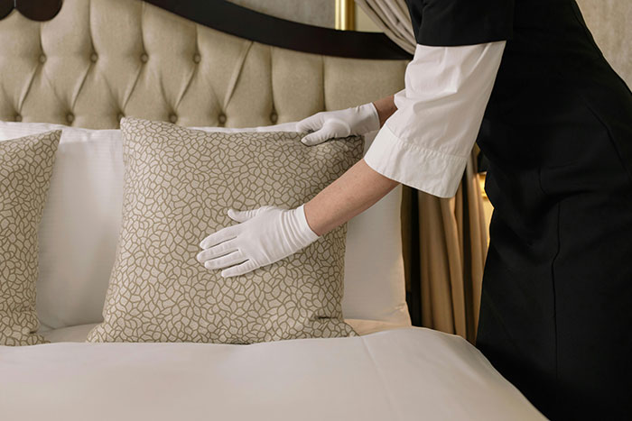A gloved person arranges luxury pillows on an elegant bed, showcasing what the super rich can buy with money.