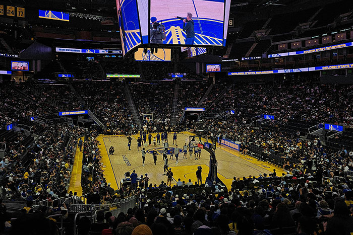 A packed basketball arena with spectators and a large screen displaying the court, showcasing luxury experiences money can buy.