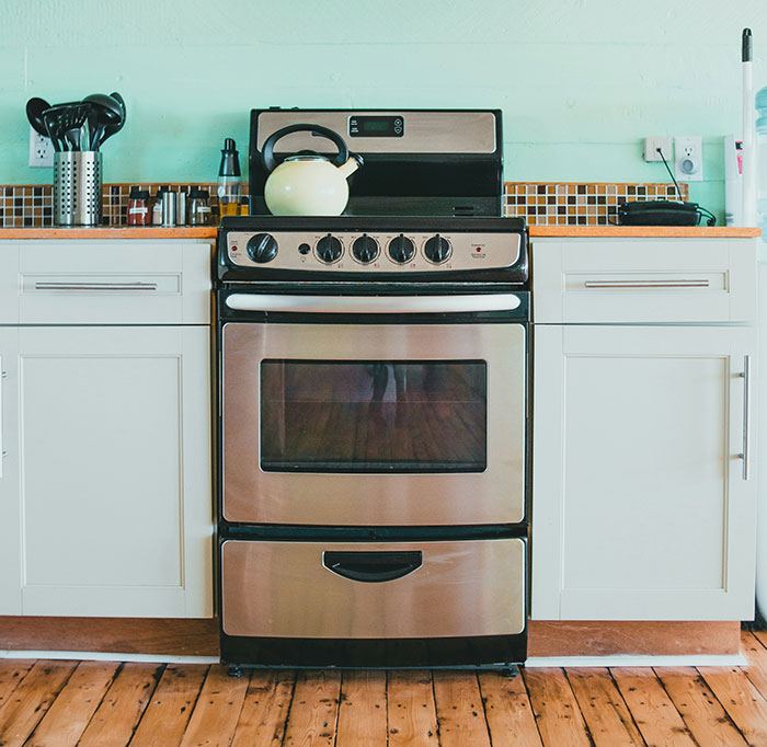 Stainless steel stove with a kettle on top, surrounded by kitchen cabinets.