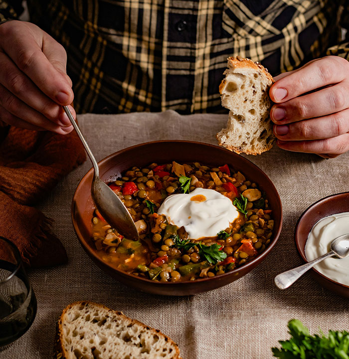 A person enjoys a hearty lentil soup with yogurt and bread, symbolizing comfort amidst possible weaponized incompetence.