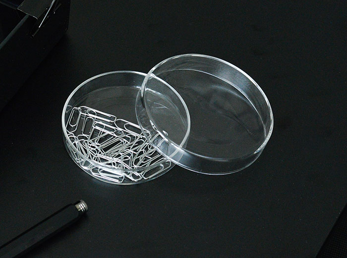 Open container with paperclips, suggesting weaponized incompetence in office organization on a dark surface.