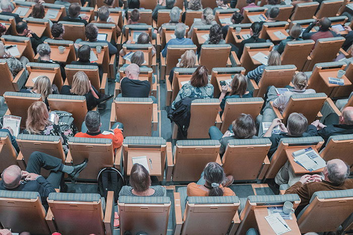 Audience in a lecture hall with papers, viewed from above.