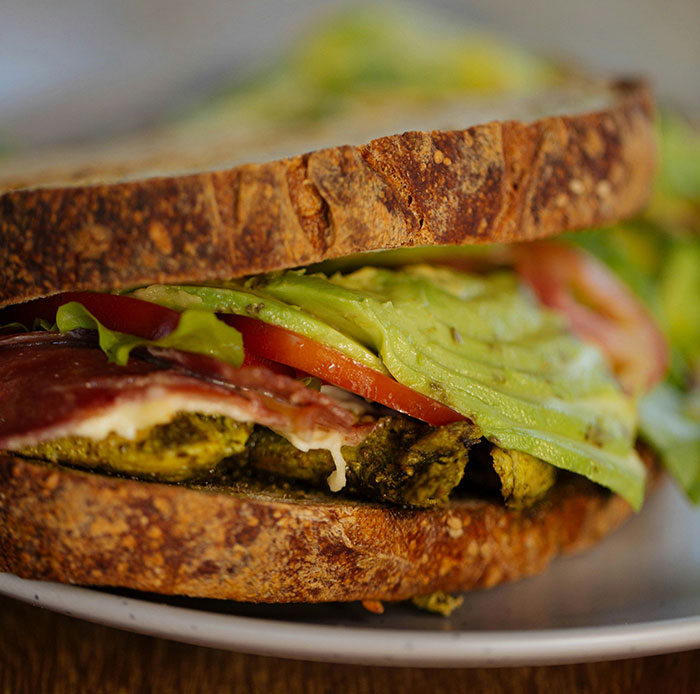 Sandwich with avocado, tomato, and meat, poorly assembled, illustrating weaponized incompetence in food preparation.
