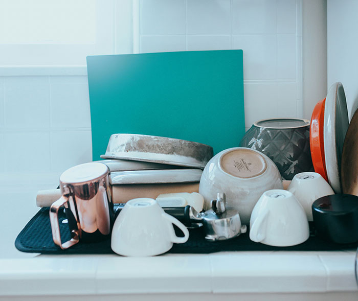 Dishes and mugs cluttered on a drying mat, symbolizing household weaponized incompetence.